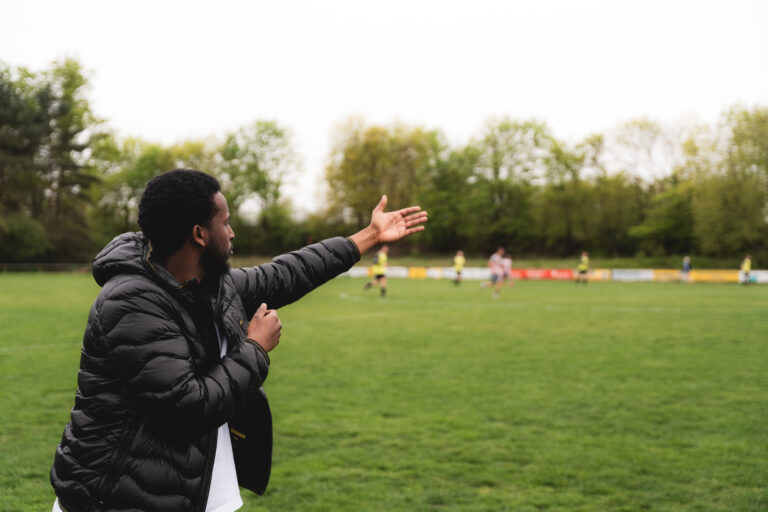 Ein Mann im schwarzen Trainingsanzug gestikuliert am Spielfeldrand.