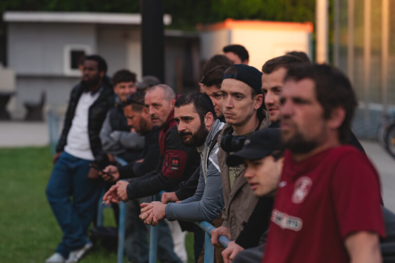 Zuschauer und Mannschaftsmitglieder verfolgen das Spiel am Spielfeldrand.