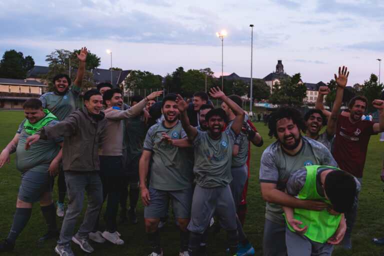 Spieler der SpG Nordweststadt 2 stehen lachend mit erhobenen Armen zusammen auf dem Platz.